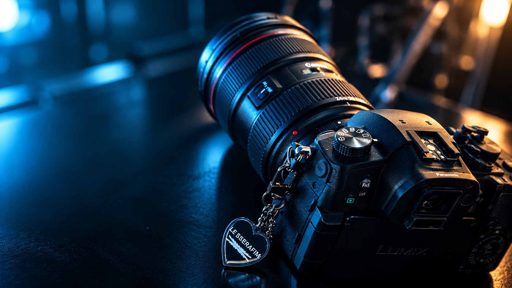 A Lumix camera with a Canon zoom lens on a dark table, lit in blue and amber
