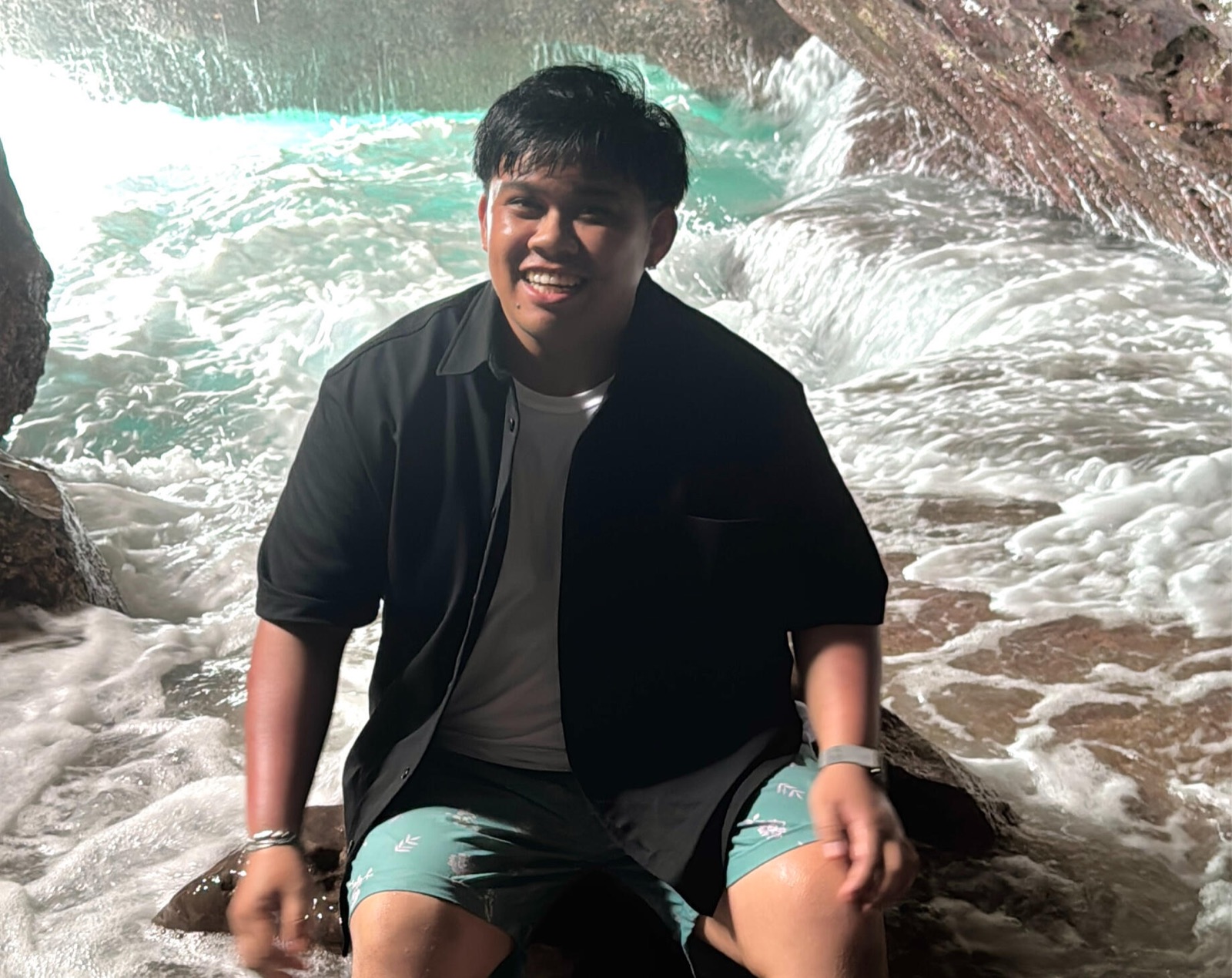 Ryan of Fear Not Video Creative, smiling on a rock in a sea cave as waves crash behind